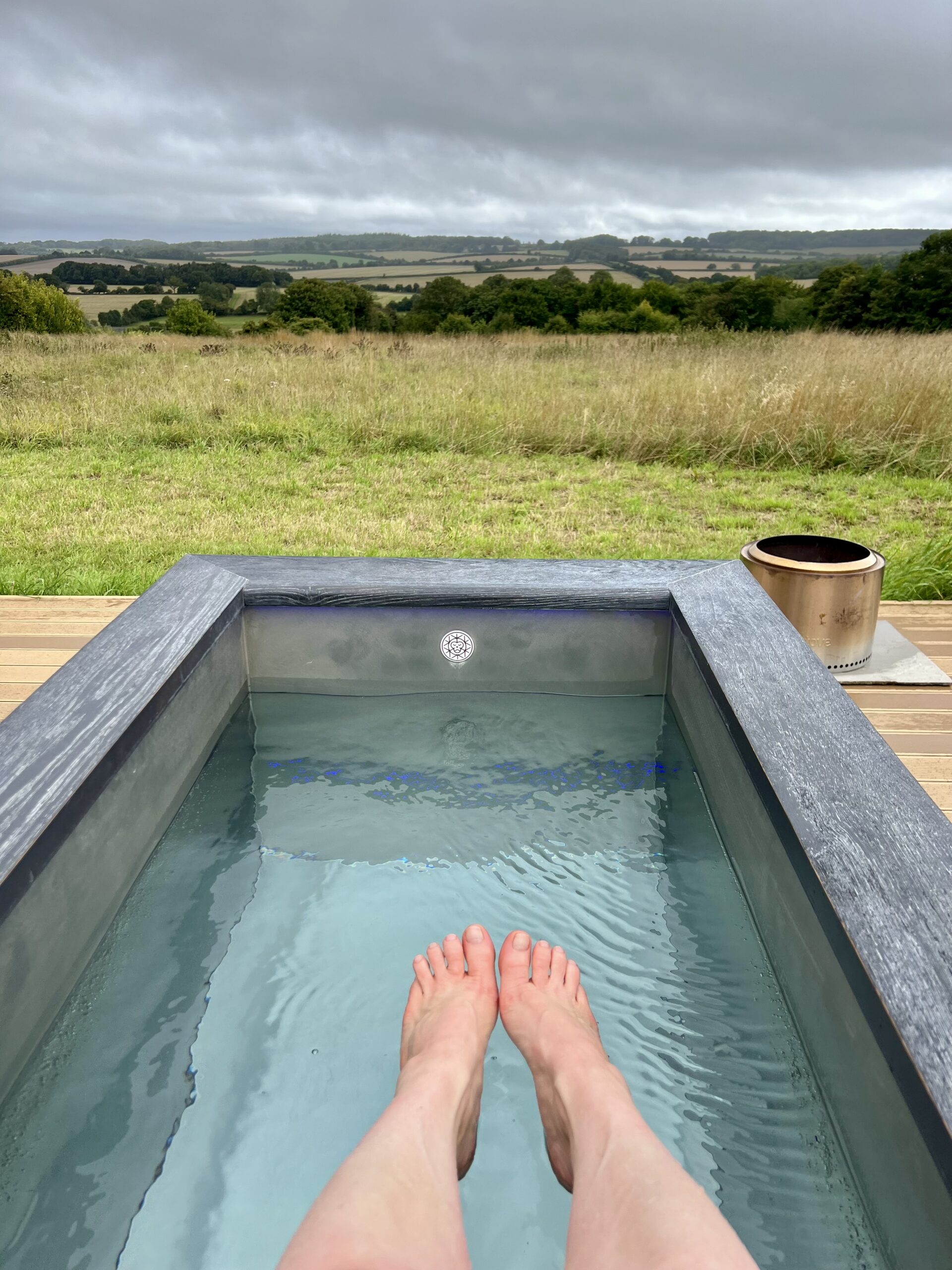 My feet hovering over the cold water of the ice bath, with the view of the surrounding fields.
